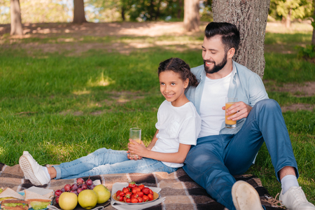 father and daughter drinking juice while sitting on plaid at picnicの写真素材