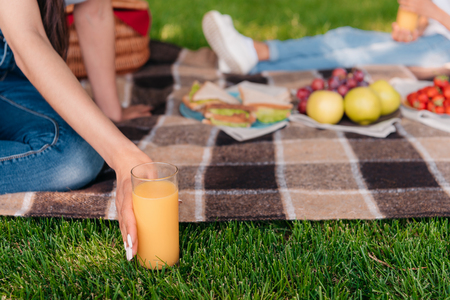 Cropped shot of person holding glass with fresh juice while sitting on plaid at picnicの写真素材