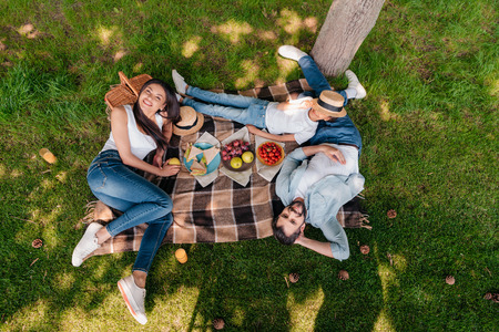 multiethnic family eating and drinking while resting on plaid at picnicの写真素材