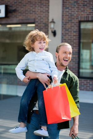 happy father holding little son with shopping bags in handの写真素材
