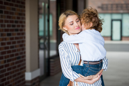 son hugging smiling mother while sitting in her handsの写真素材