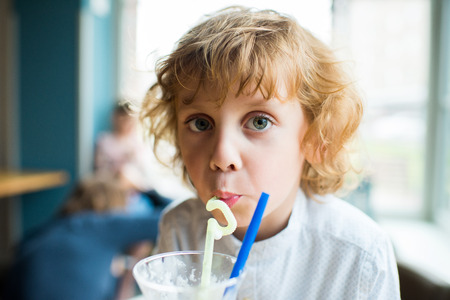 kid boy with curly hair drinking milkshake and looking at cameraの写真素材