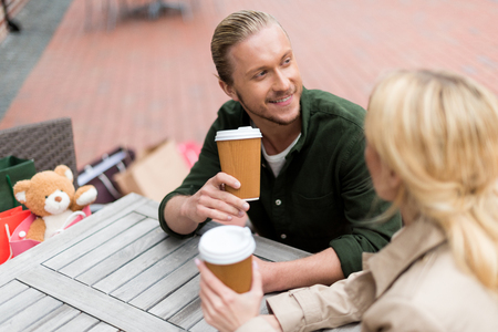 man talking with his girlfriend while drinking disposable coffee at cafeの写真素材