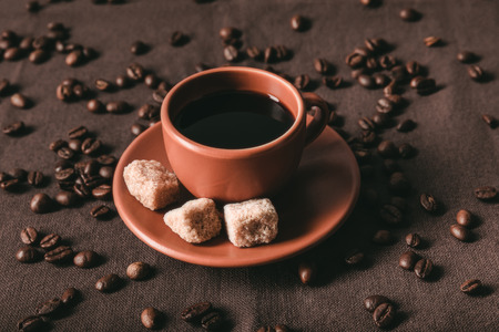 ceramic coffee cup with brown sugar cubes and scattered coffee grains on brown clothの写真素材