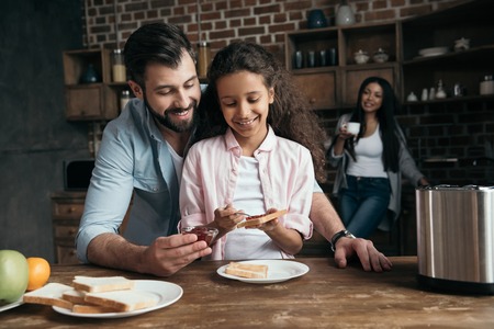 father helping little daughter preparing toasts with jamの写真素材
