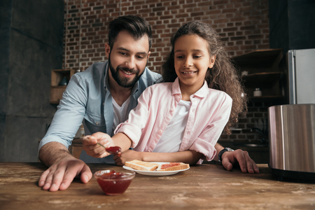 father and daughter eating toasts with jam in kitchenの写真素材