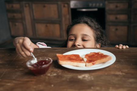 little girl looking at jam in bowl on tableの写真素材