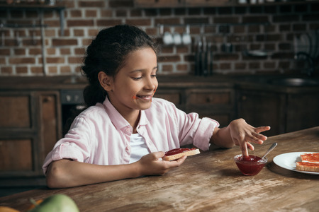 adorable girl with toast in hand playing with jam in bowlの写真素材