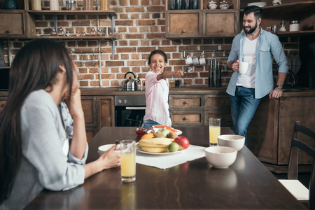 girl playing with spoon in hand while family having breakfastの写真素材