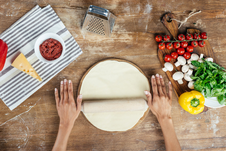 female hands rolling pizza dough with pin on tableの写真素材