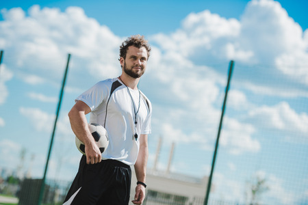 referee holding soccer ball while standing on soccer pitchの写真素材