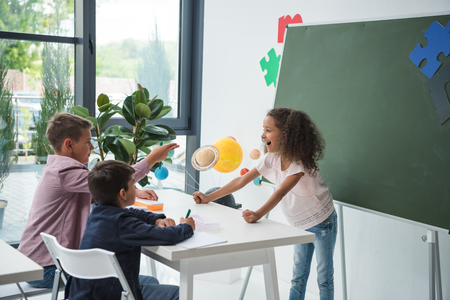 multiethnic schoolchildren talking and smiling at desk in classroomの写真素材