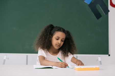 african american pupil writing in exercise book at lesson in classの写真素材