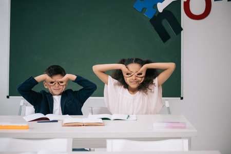 multiethnic pupils having fun while sitting together at desk in classの写真素材