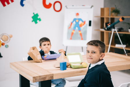 caucasian schoolboys eating lunch while sitting at wooden table