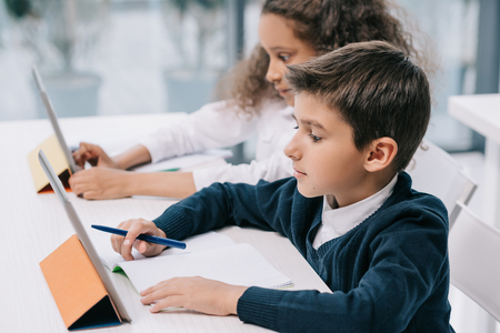 focused multiethnic schoolchildren using digital tablets while studying in classroomの写真素材