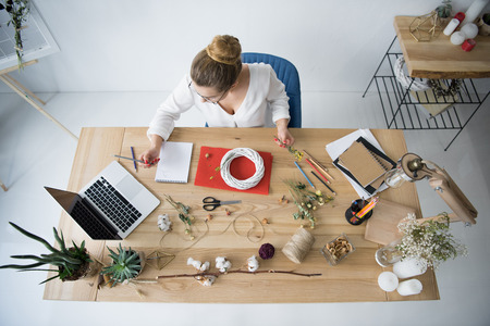 female decorator with wreath, dry flowers and laptop at workplaceの写真素材
