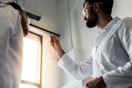 male scientists in white coats holding test tube with reagent in chemical labの写真素材