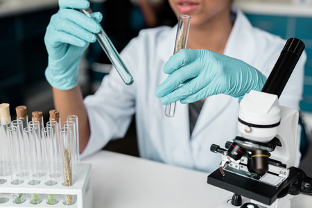 scientist in white coat examining test tubes while making experiment in chemical labの写真素材
