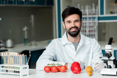 young scientist examining vegetables and smiling at camera in laboratoryの写真素材