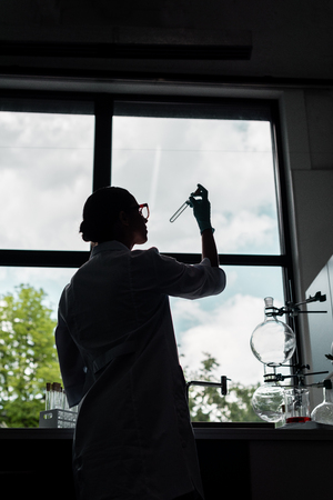 young scientist in eyeglasses and white coat holding test tube in chemical labの写真素材