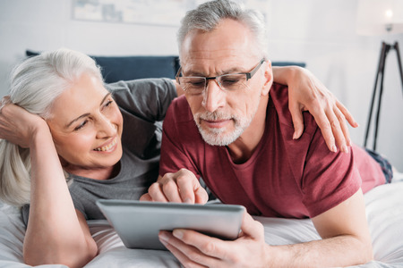 senior couple with digital tablet resting in bed together