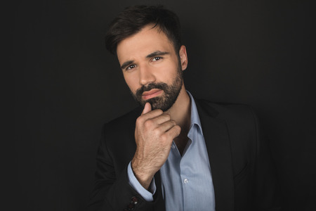handsome bearded pensive businessman posing in black suitの写真素材