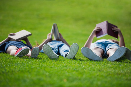 Children lying on grass together and reading booksの写真素材