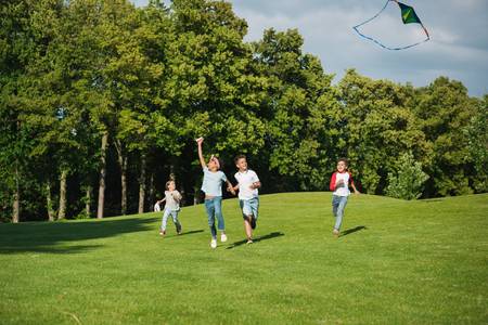 multiethnic kids playing together while running with kite in parkの写真素材