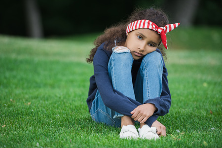 little african american girl sitting on green grass and looking at cameraの写真素材