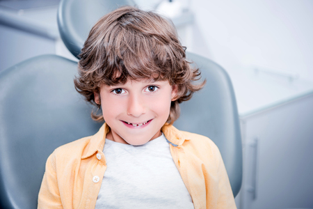 smiling boy sitting in chair in dentist officeの写真素材
