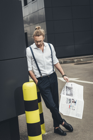 stylish young businessman in eyeglasses reading newspaper and looking downの写真素材