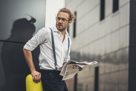 stylish young businessman in eyeglasses reading newspaper and looking awayの写真素材