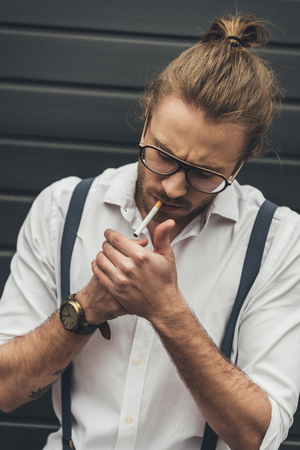 handsome stylish man in eyeglasses lighting cigarette with lighterの写真素材