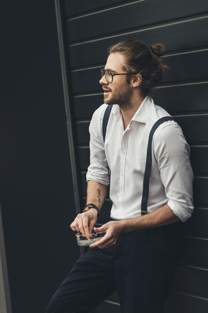 stylish young man in spectacles holding ashtray while smoking and looking awayの写真素材