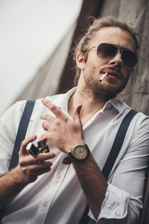 bearded handsome man in sunglasses lighting cigarette with lighterの写真素材