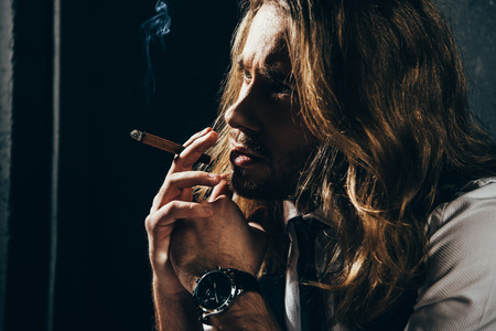 pensive bearded young man smoking cigar and looking awayの写真素材