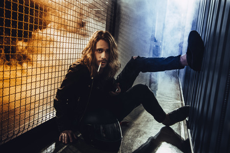 bearded long haired man in leather jacket smoking cigarette and looking at cameraの写真素材