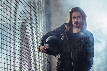 long haired bearded man in leather jacket holding helmet and looking at cameraの写真素材