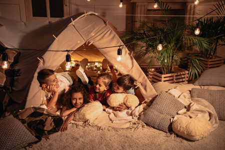 children resting in handmade tent together at homeの写真素材