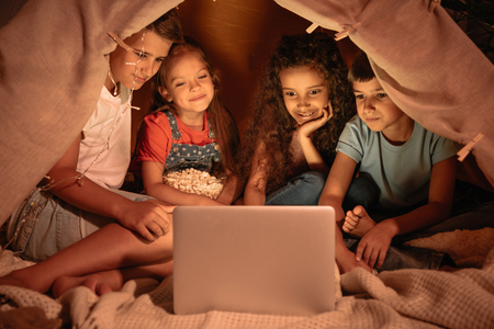 multiethnic kids sitting tent and watching film togetherの写真素材