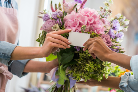 female hands holding blank business card and bouquet of beautiful flowersの写真素材