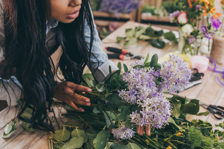 young african american woman arranging flowers and green leaves in flower shopの写真素材