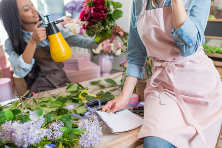 young florists in aprons working together in flower shopの写真素材