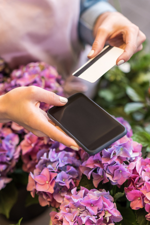 person holding smartphone and credit card while standing in flower shopの写真素材