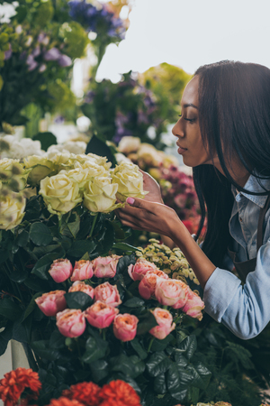african american woman smelling beautiful roses in flower shopの写真素材