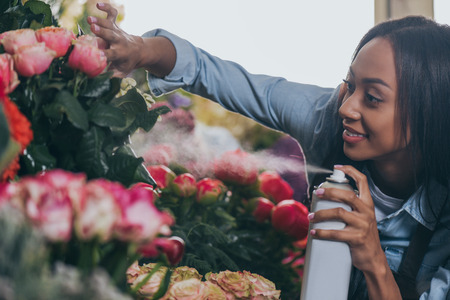 young african american florist spraying beautiful flowersの写真素材