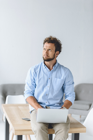 businessman sitting on table with laptop on knees in officeの写真素材