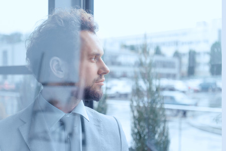 thoughtful businessman in suit looking out window in office