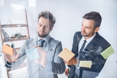businessmen putting sticky notes on glass while working in officeの写真素材